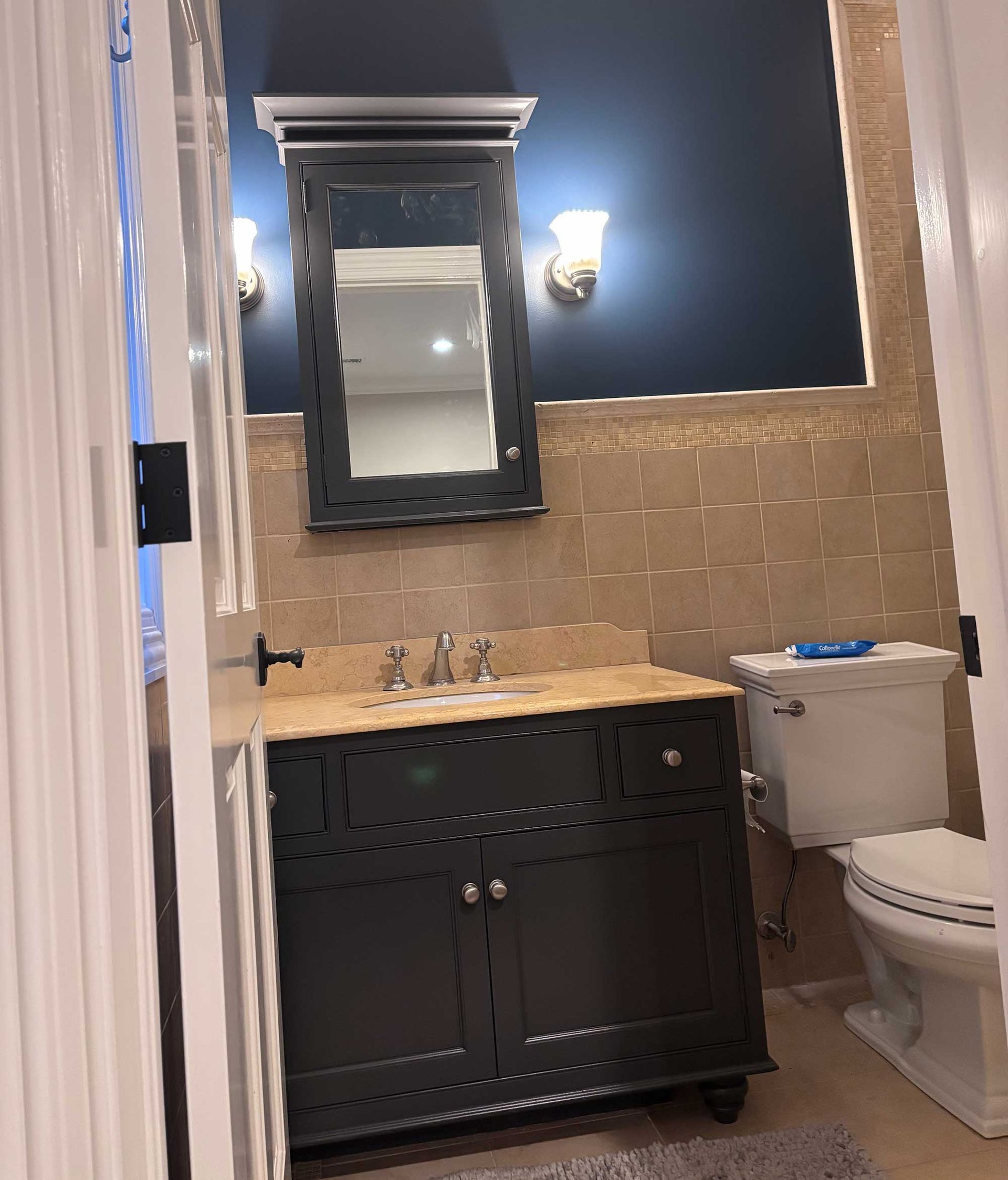 Bathroom with a dark vanity, tan backsplash, blue wall, and white toilet.