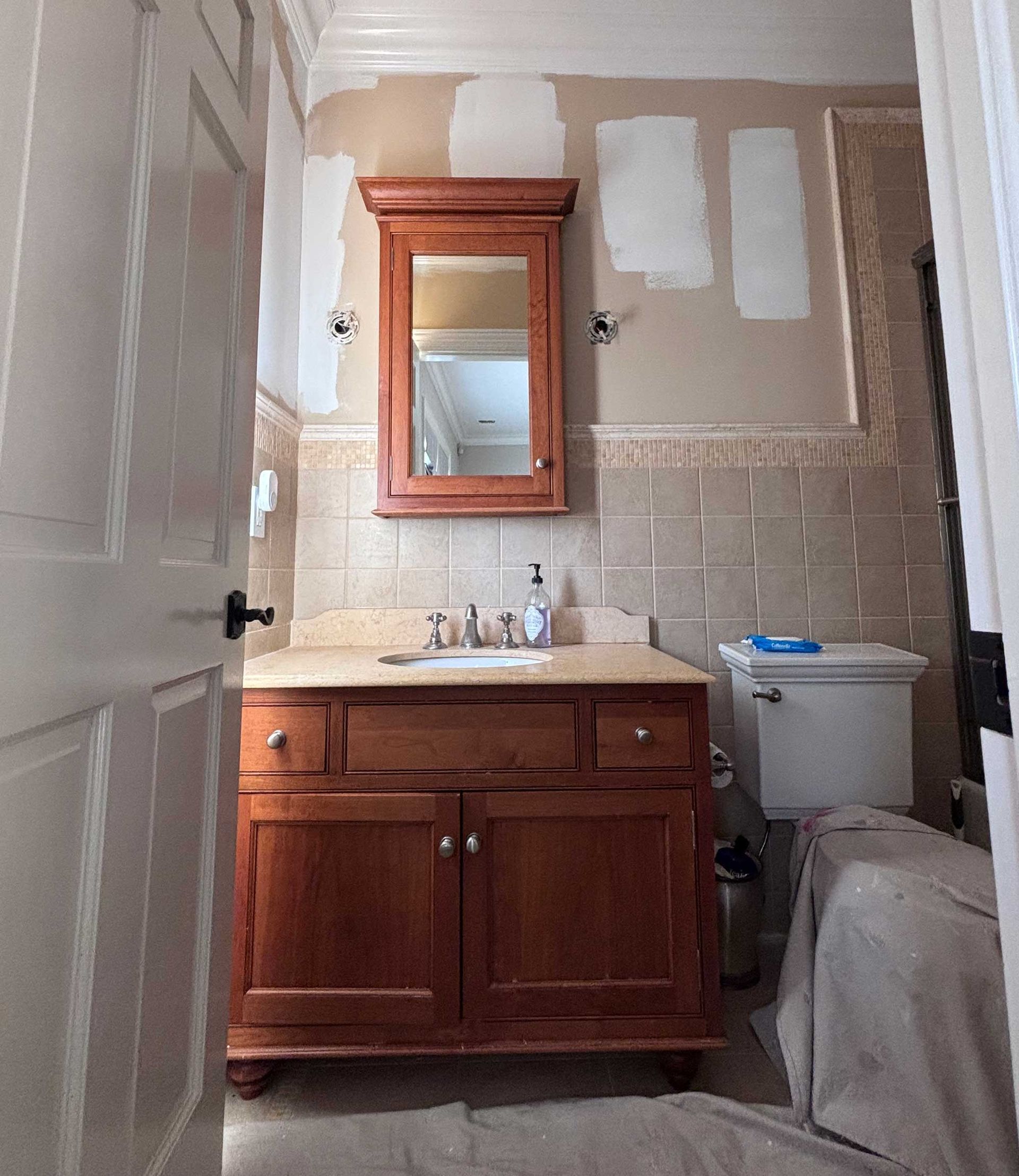 Bathroom interior with wooden vanity, medicine cabinet, and toilet; walls are partially painted.