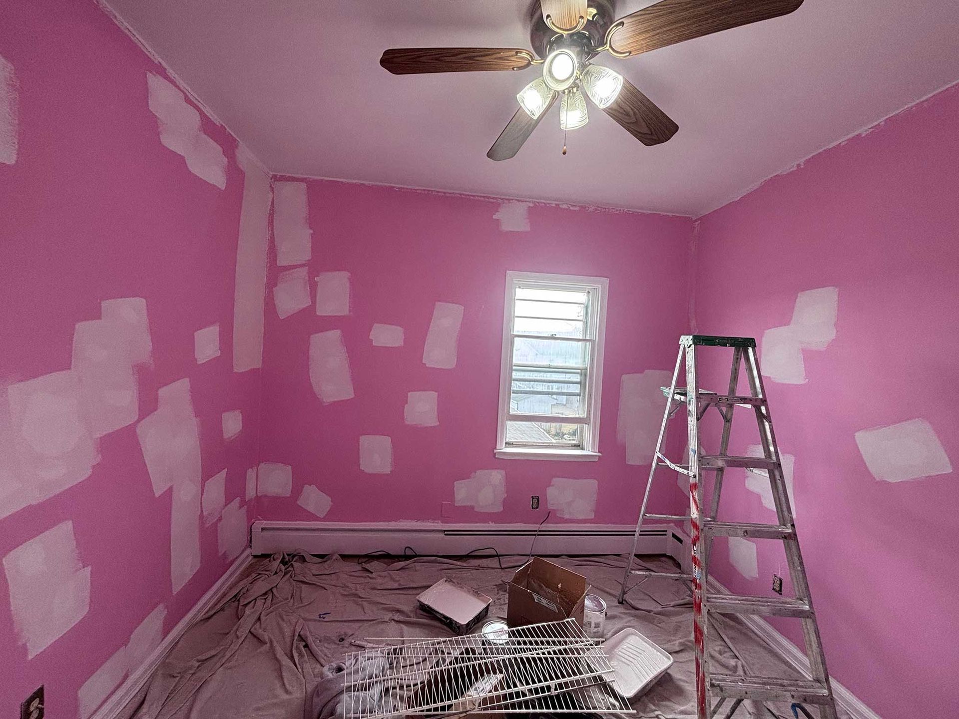Room being painted pink, with patches of white primer. Ladder present near the window.