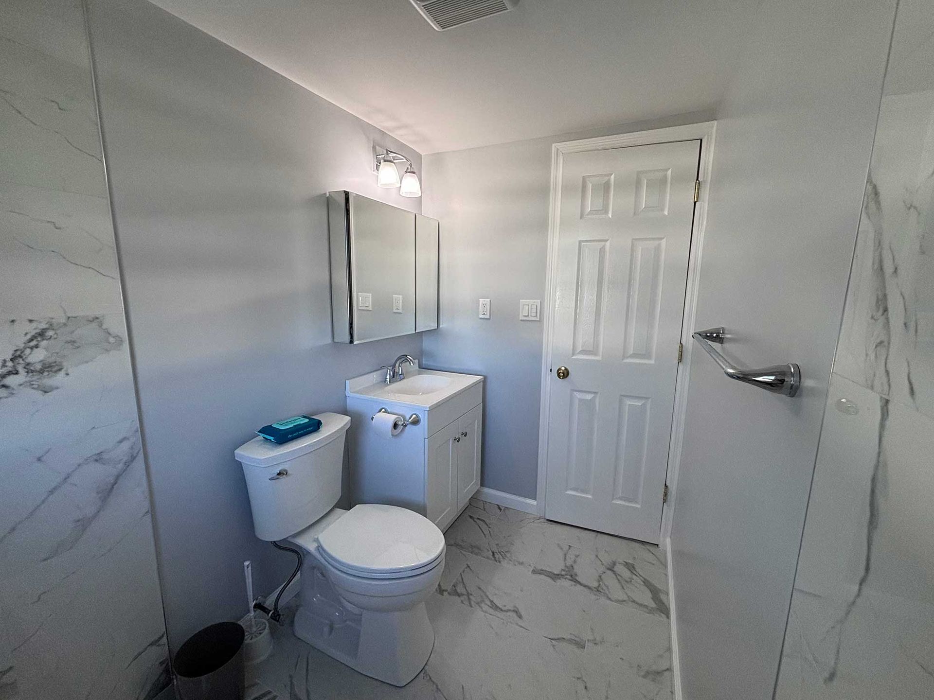 Modern bathroom with white and gray marble tile, white vanity, and toilet.
