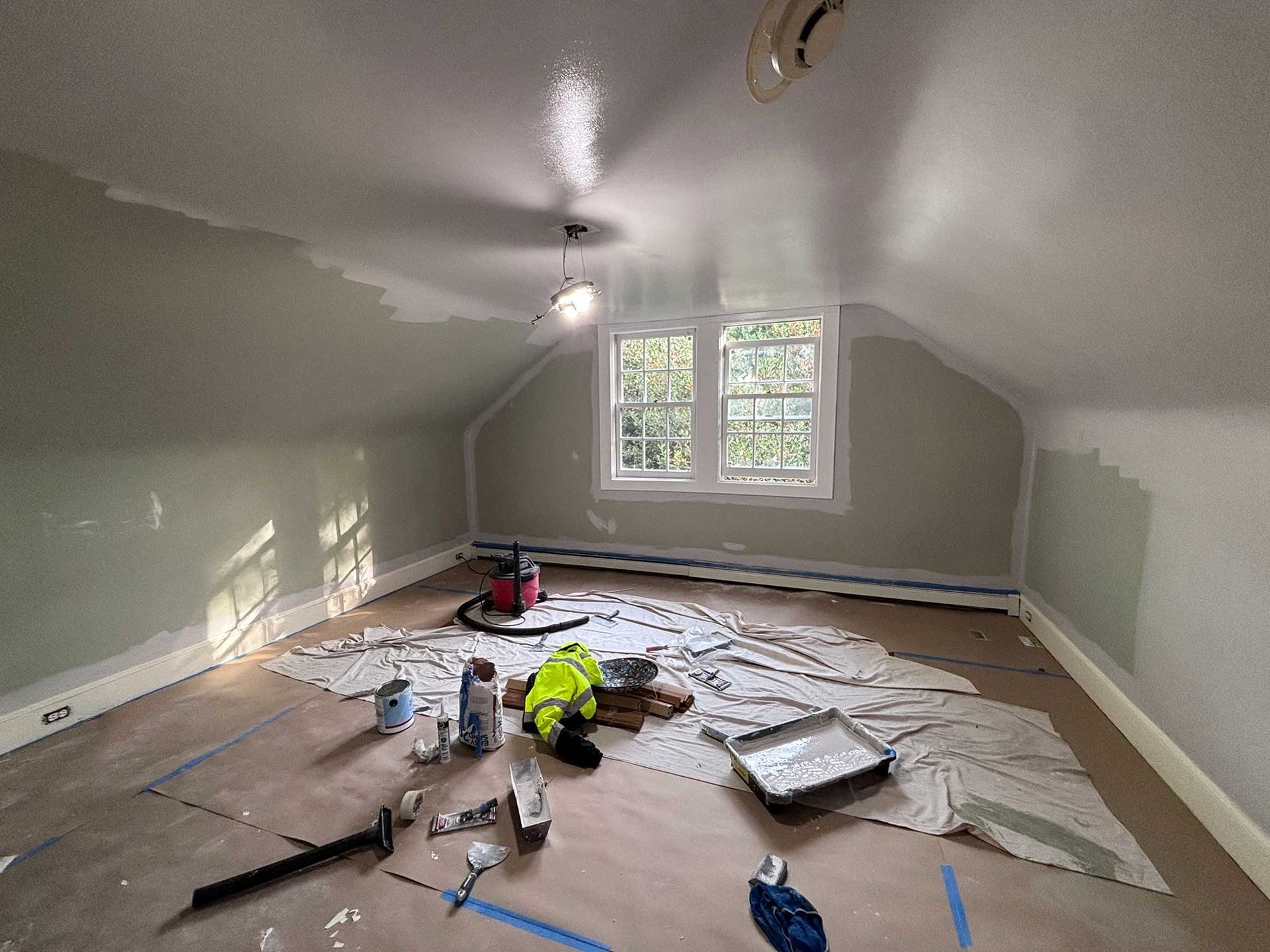 Room under renovation with paint supplies, a window, and partially painted walls.