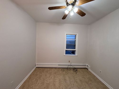 Empty bedroom with beige carpet, white walls, ceiling fan, and a small window at the far end.