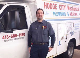 Plumber standing beside a white service van with “Hodge City Mechanical Plumbing & Heating” signage.