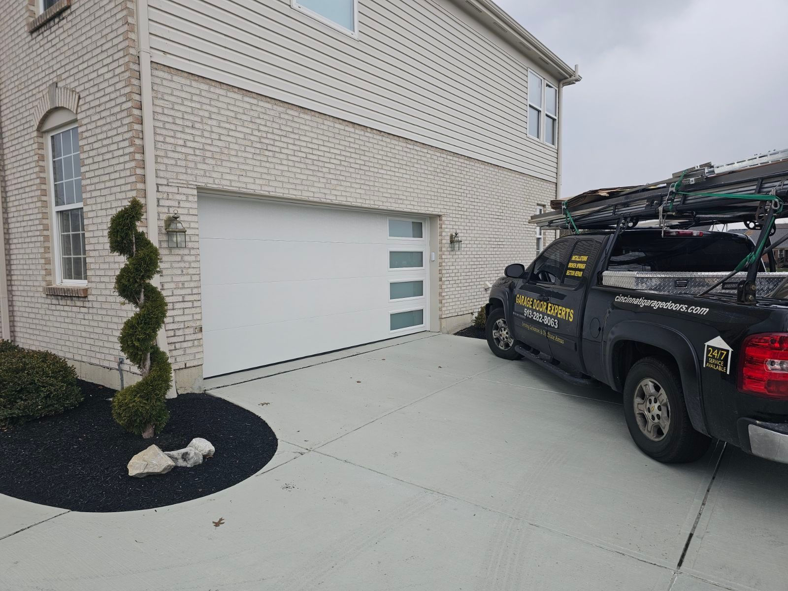 Driveway beside a beige house with a white garage door and a black work truck parked on the right.