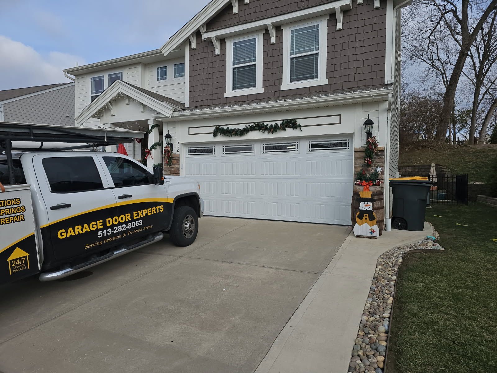 Garage door service van parked in a suburban driveway beside a two-story house.