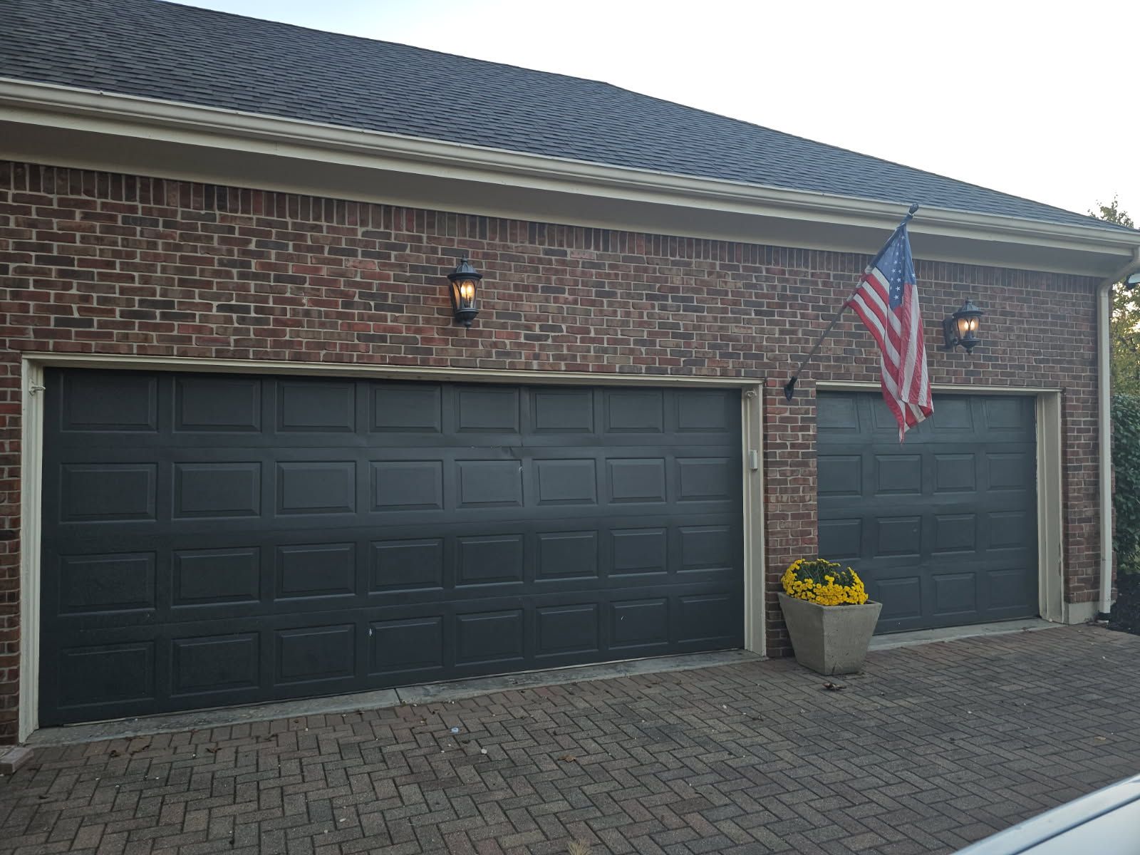 Brick house with two black garage doors, a U.S. flag, and a planter by the driveway.