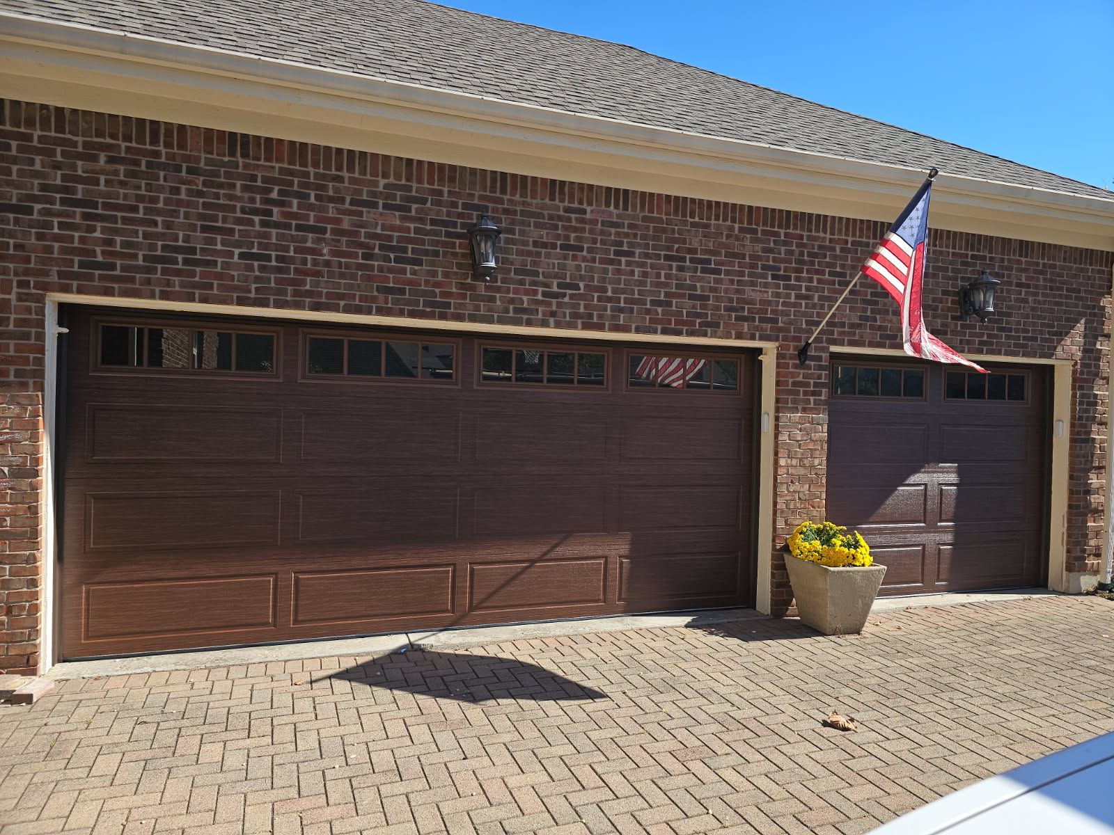 Brick house garage with brown doors, American flag, and potted flowers on a paved driveway