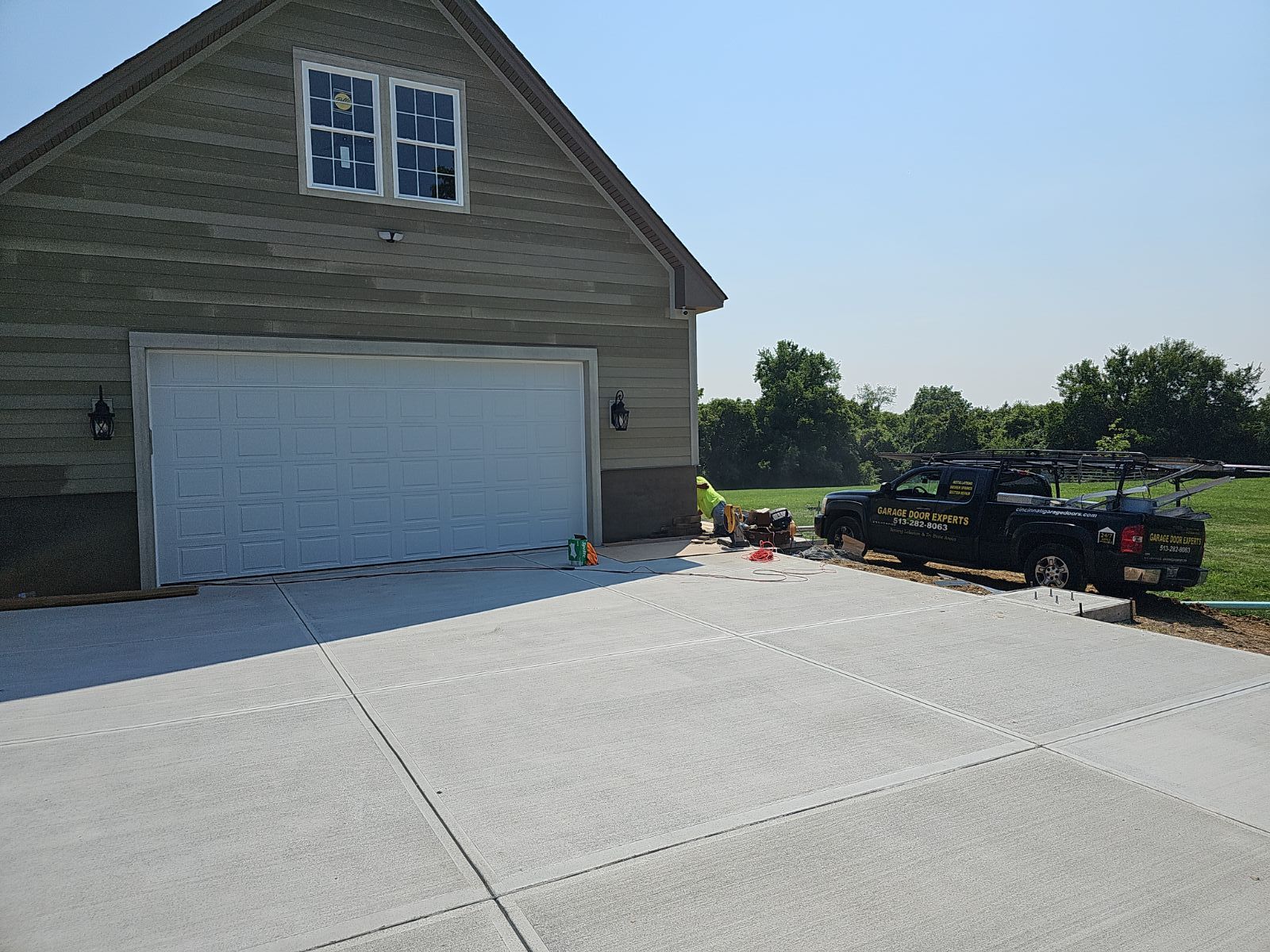 Large concrete driveway in front of a garage, with a pickup truck and landscaping materials on the right.