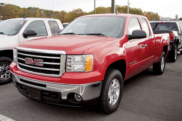 Red GMC pickup truck parked at a dealership lot, front three-quarter view.