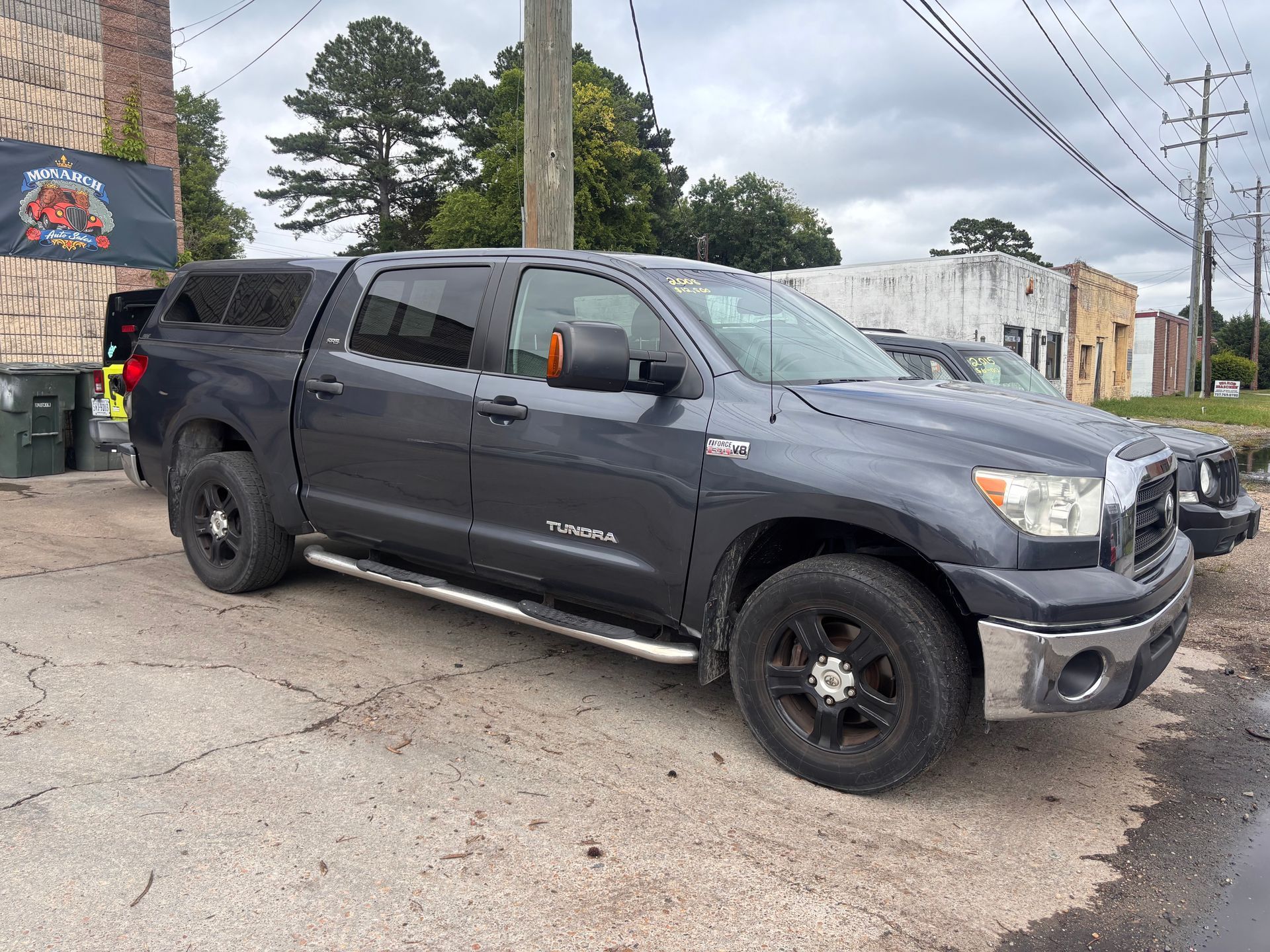 Dark gray pickup truck parked on a street beside a brick building and utility poles.
