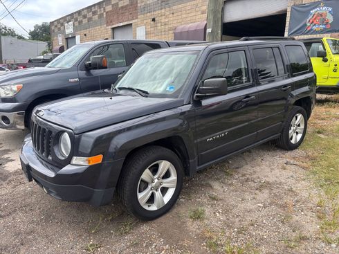 Black Jeep SUV parked outside a stone garage, with a dark van and a yellow vehicle in the background