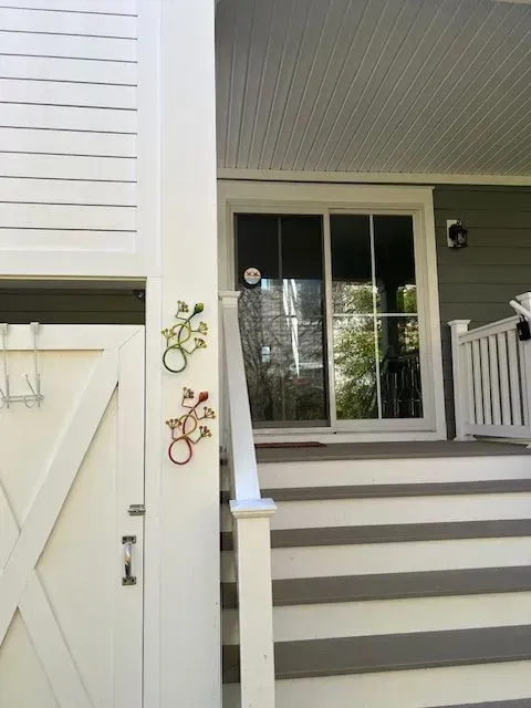 Front porch steps leading to a white door and window, with small decorative wall hangings