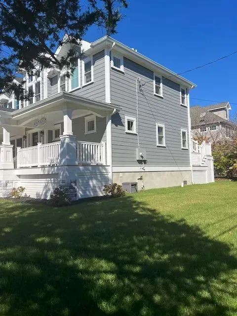 Gray two-story house with white porch and trim, viewed from a grassy yard on a sunny day