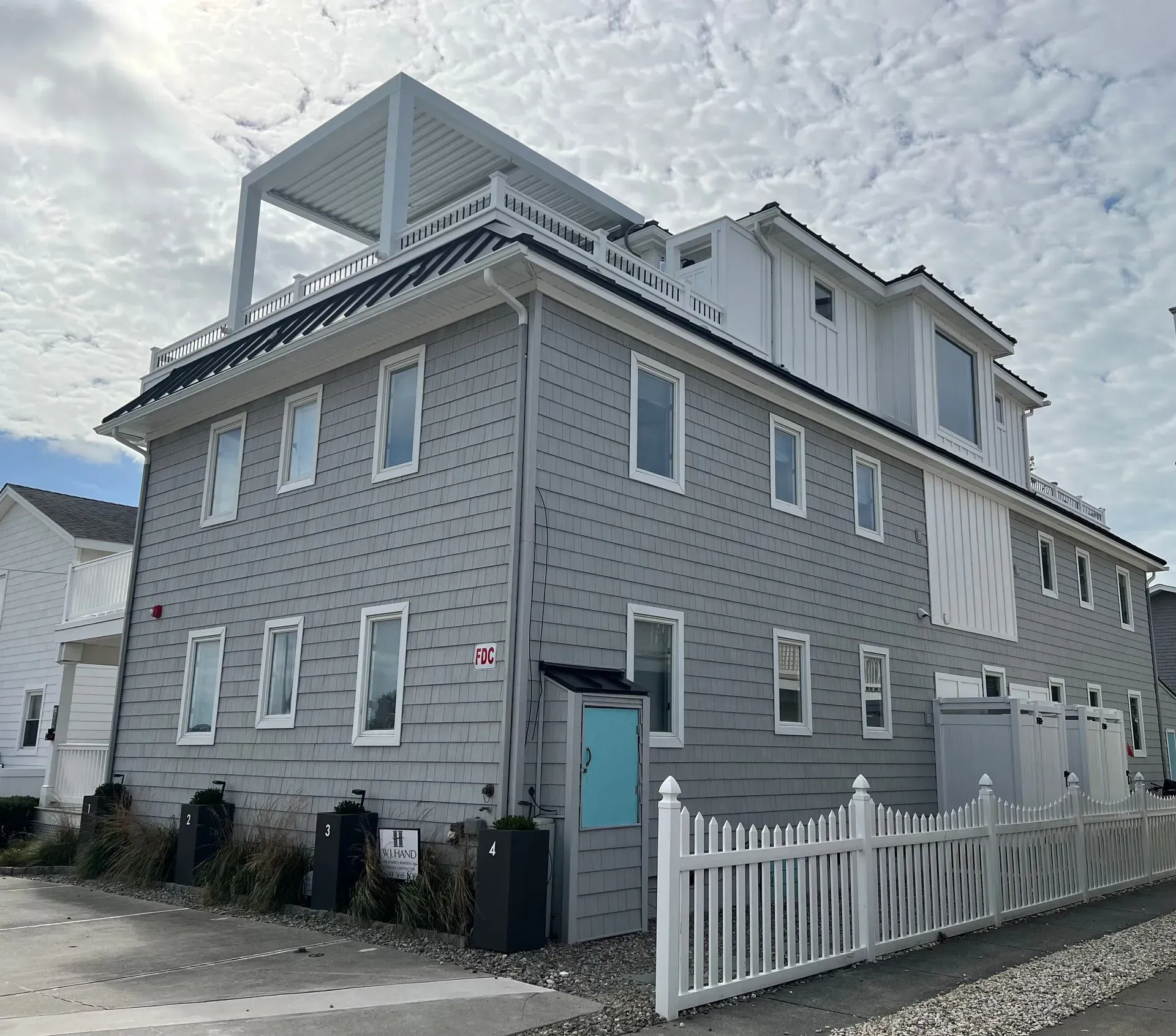 Gray two-story house with white trim and rooftop deck behind a white picket fence.