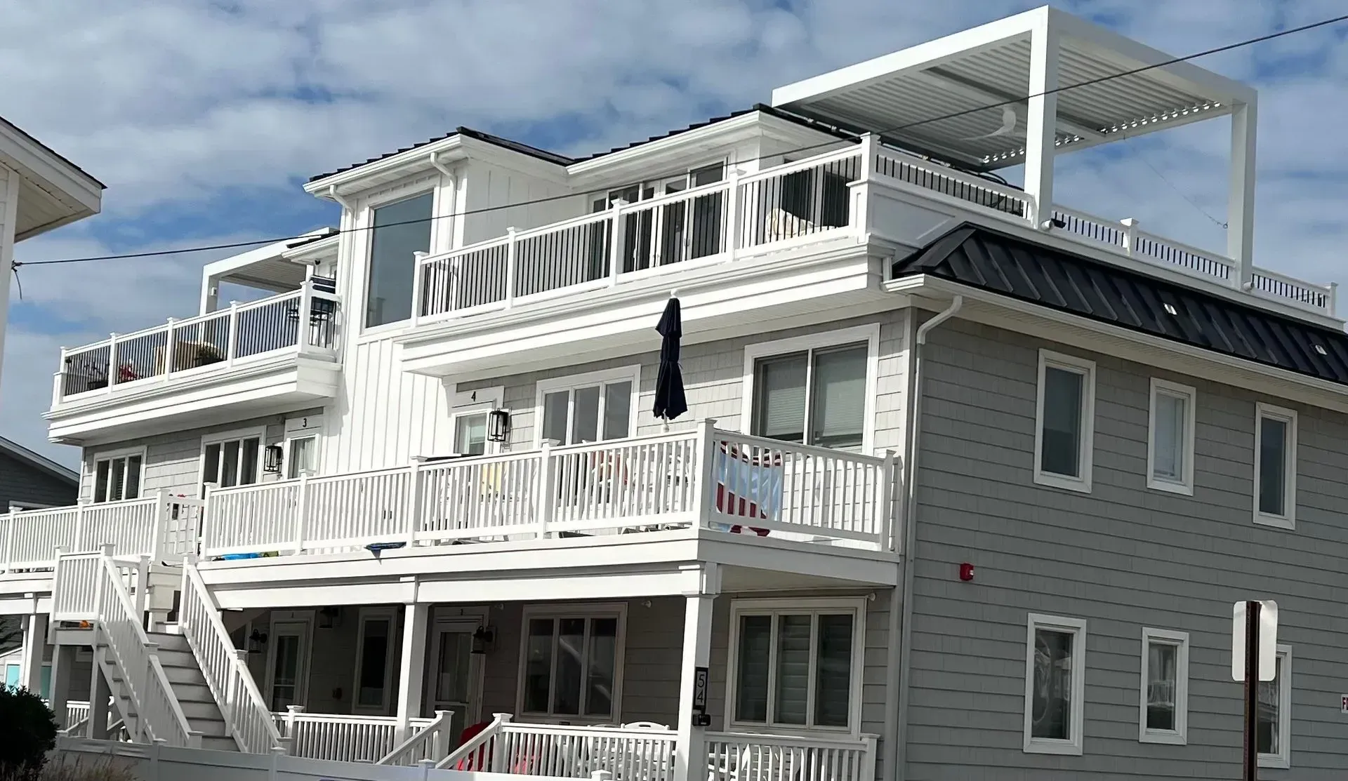 White multi-story coastal house with balconies under a partly cloudy sky