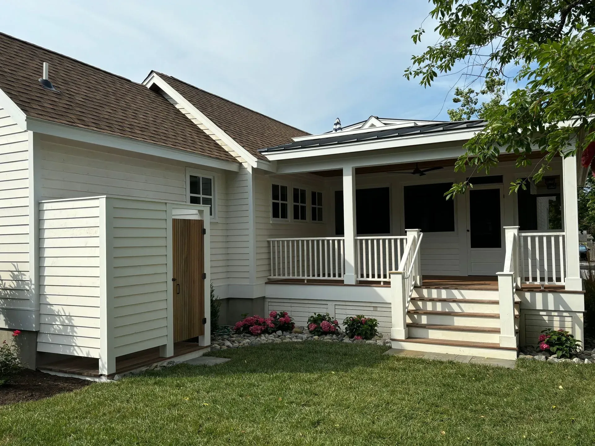 White house exterior with a front porch, steps, and flower bed under a partly cloudy sky