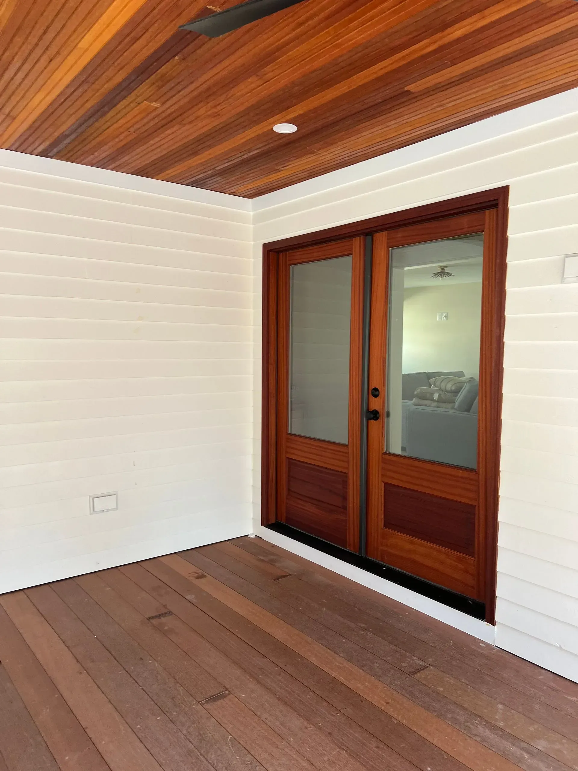 Empty room with white walls, wood ceiling and floor, and a wooden sliding glass door.