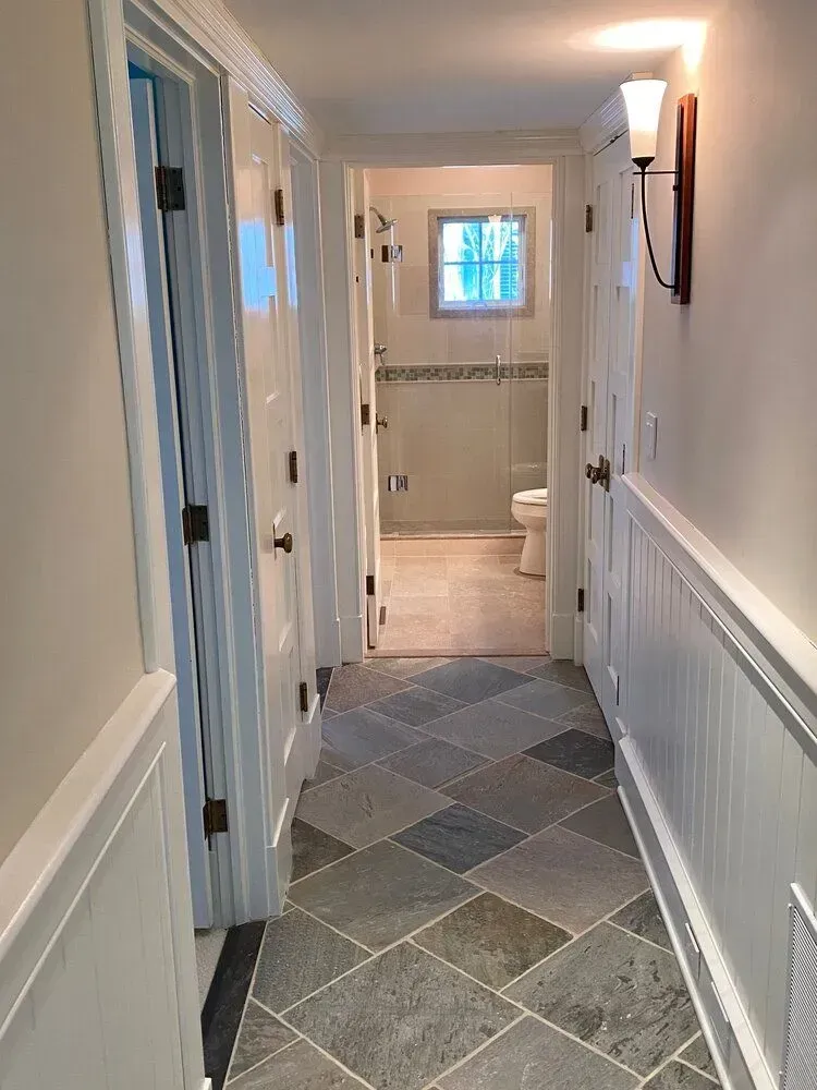 Narrow hallway with gray patterned tile, white wainscoting, and bathroom visible at the end.