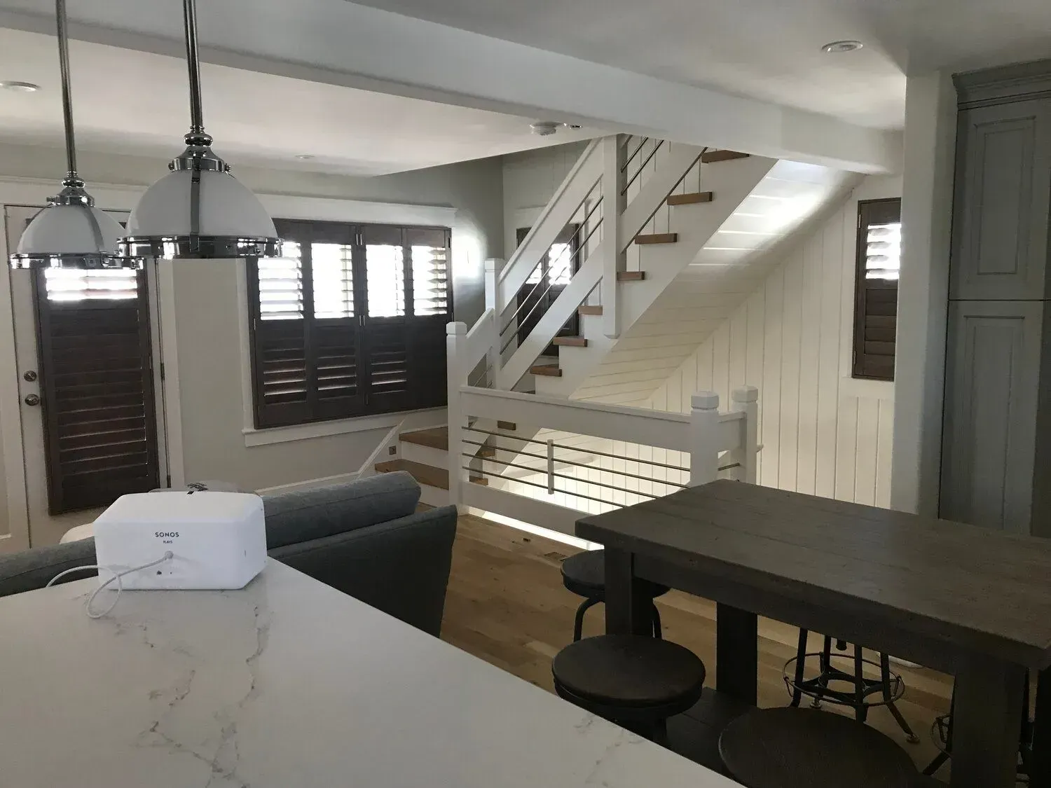 Open-plan living room with staircase, dark sofa, dining table, and kitchen island