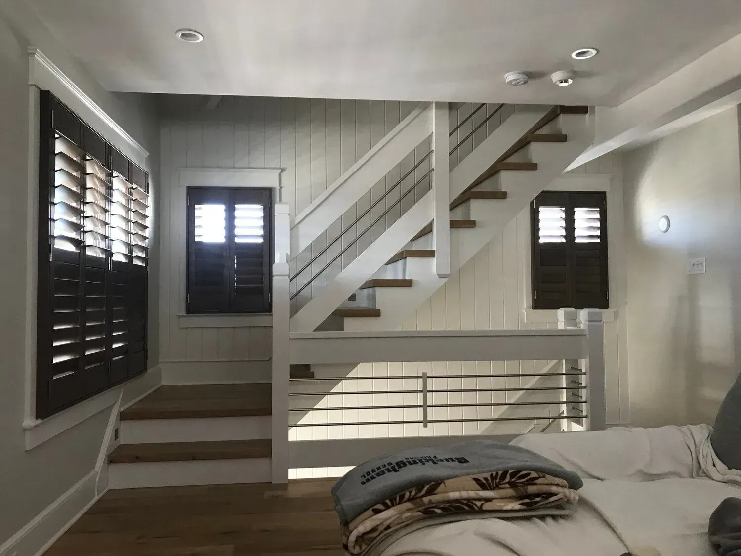 Bright bedroom with white staircase, dark shutters, and a bed in the foreground