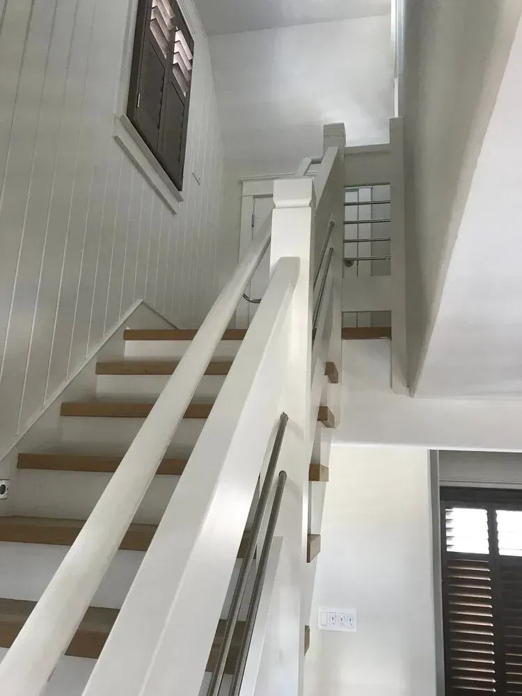 Indoor staircase with white railings and gray walls, viewed from below in a bright hallway.