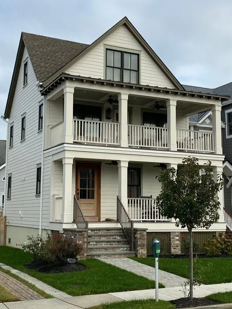 White two-story house with a front porch, balcony, and stairs on a residential street