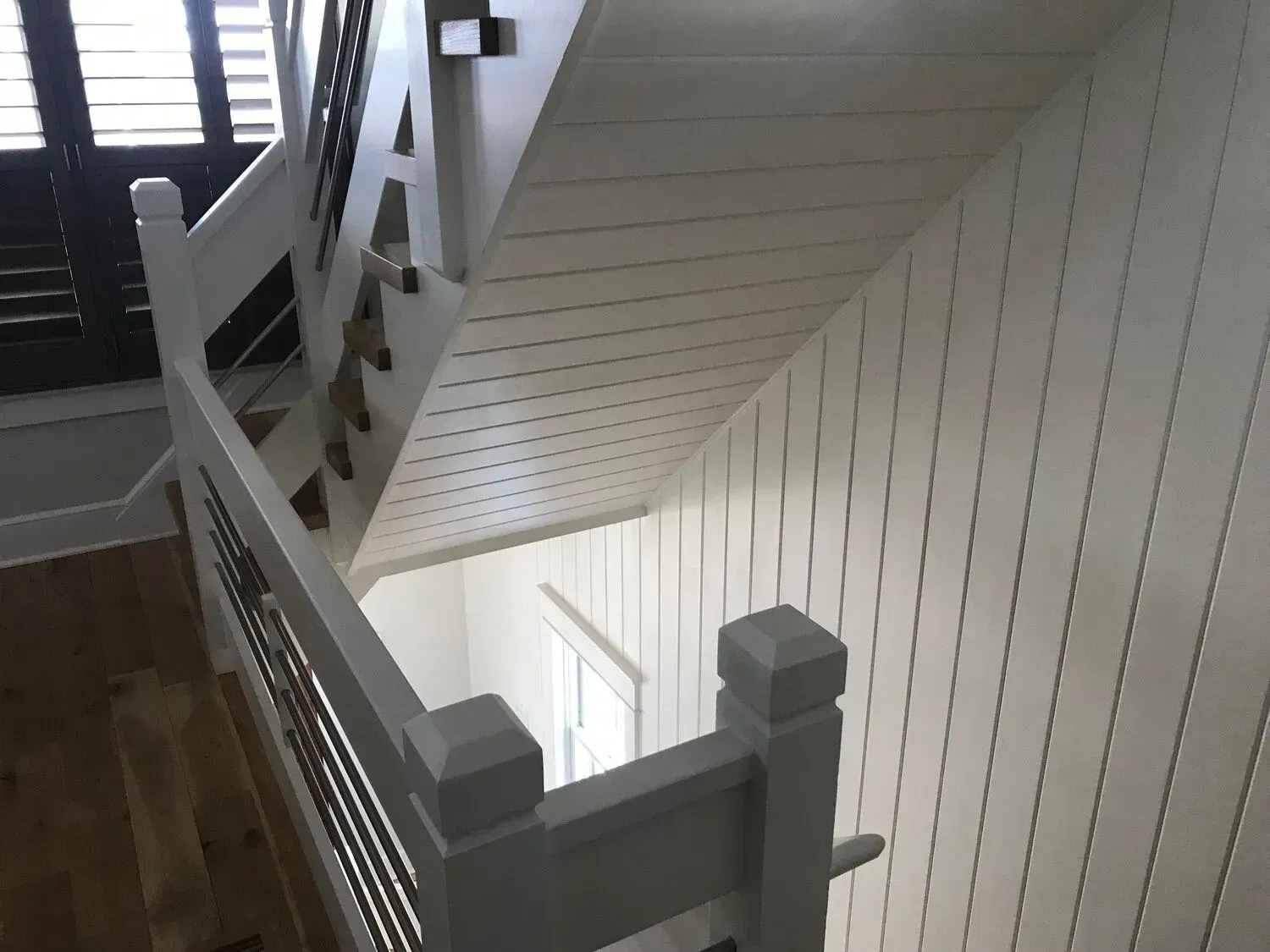Stairwell with white railings and paneled walls beside a wooden floor, viewed from above