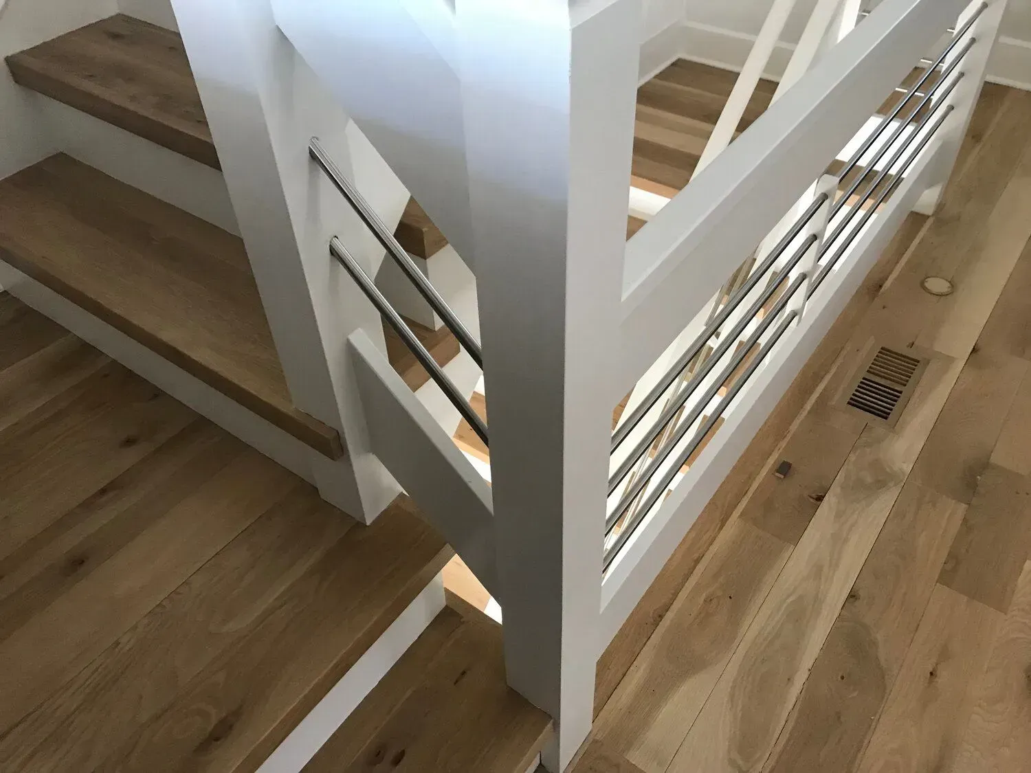 Modern stairwell with white railings, wooden steps, and a wood floor seen from above