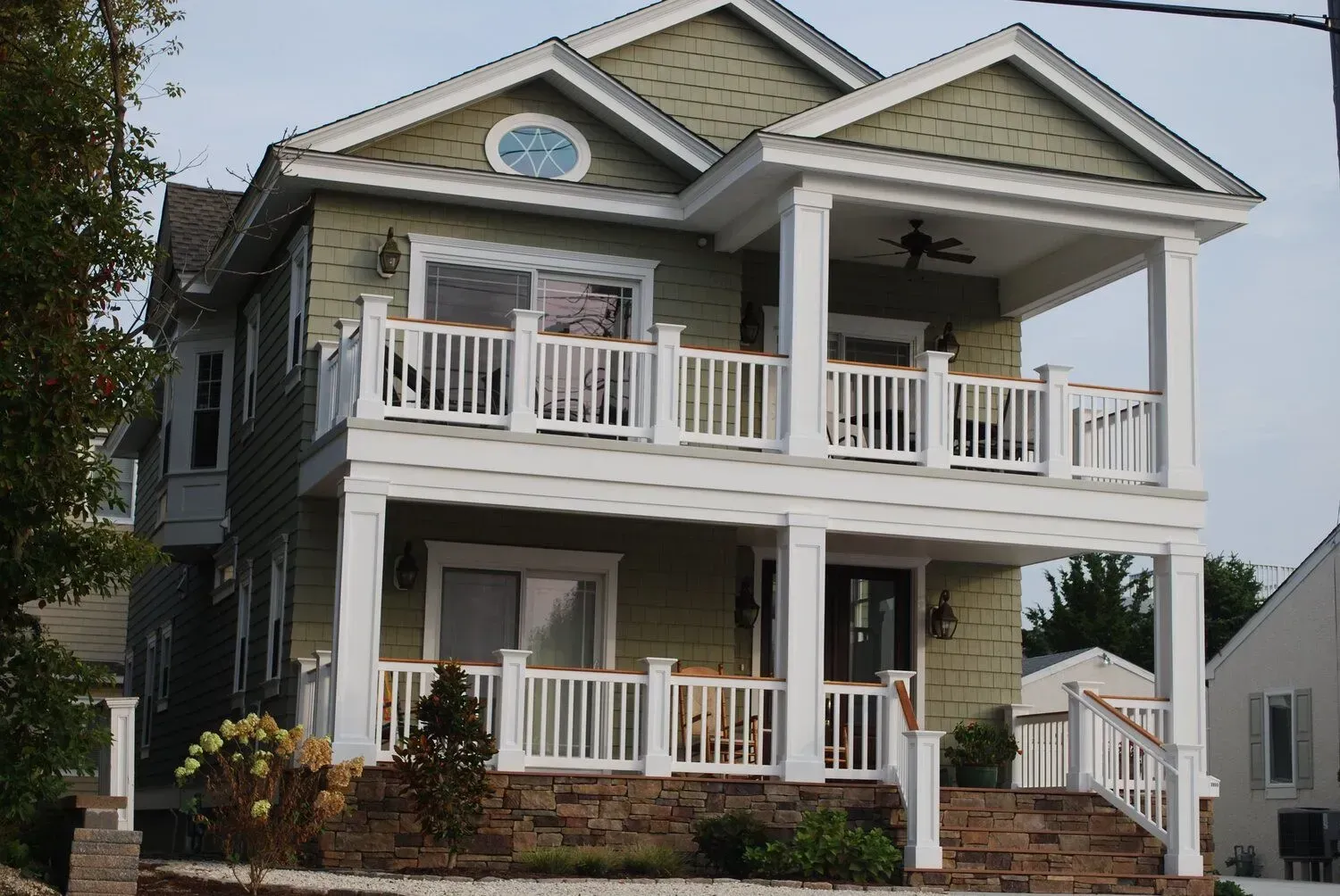 Two-story gray house with white trim, balconies, front porch, and steps leading up from the yard