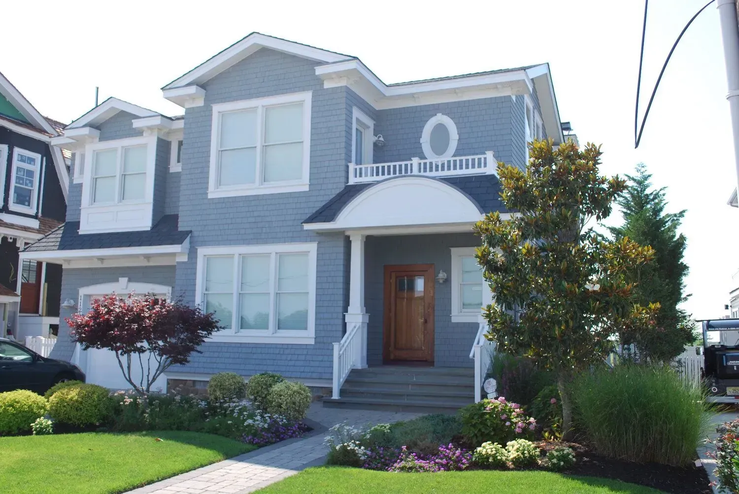 Blue-gray suburban house with white trim, front steps, and a landscaped yard on a sunny day