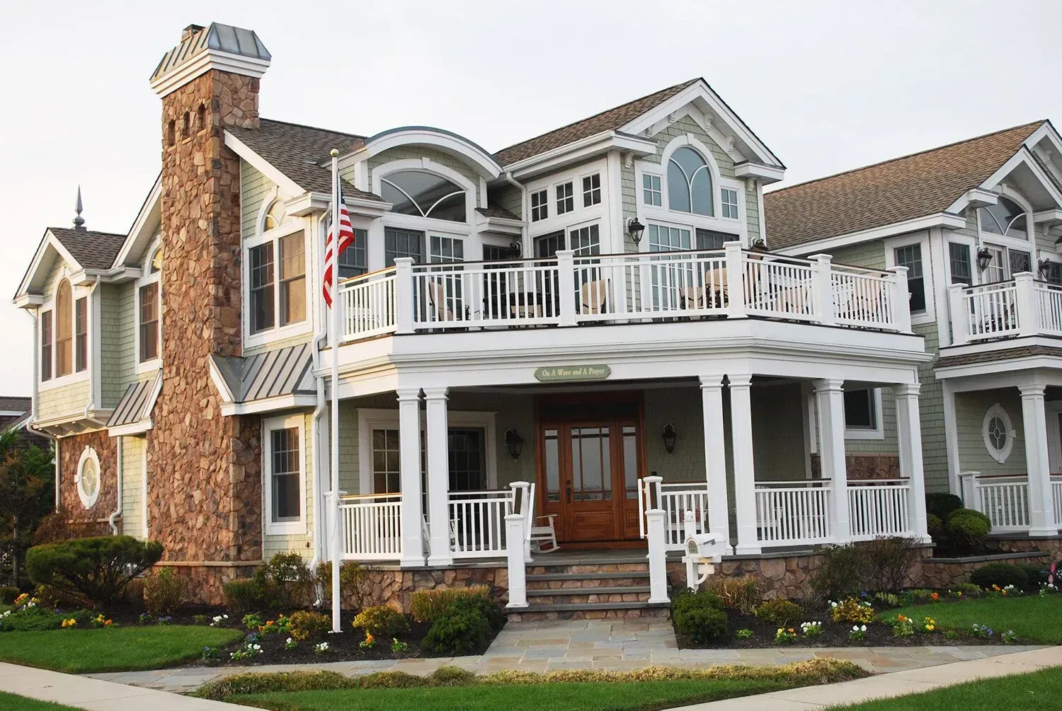 Large white seaside house with wraparound porch, arched windows, and a brick chimney