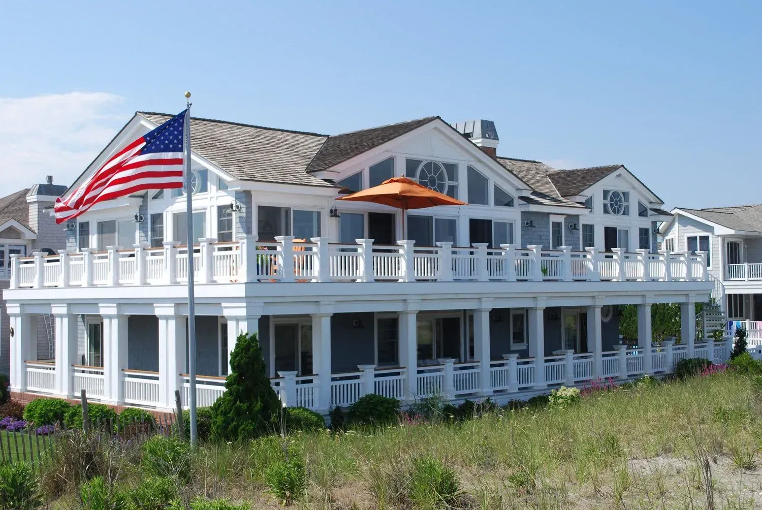 White beachfront house with wraparound porches and an American flag under a blue sky