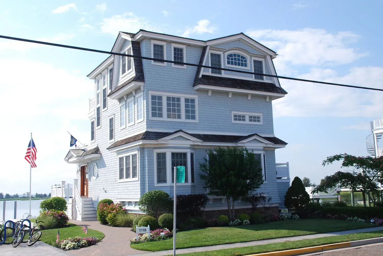 Gray coastal house with white trim, flowers, and an American flag by the waterfront