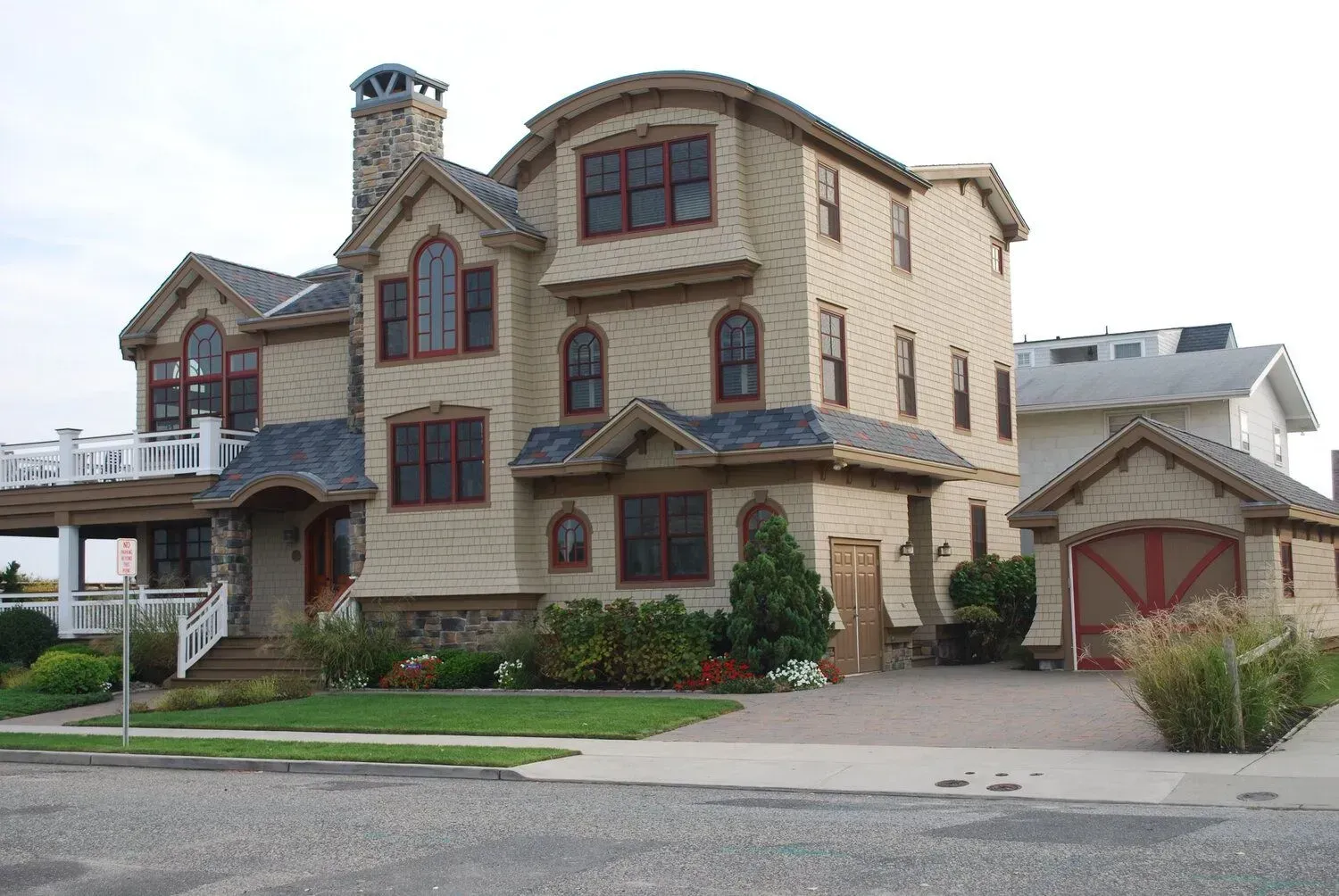 Large beige house with stone accents, red trim, a driveway, and a manicured lawn on a suburban street