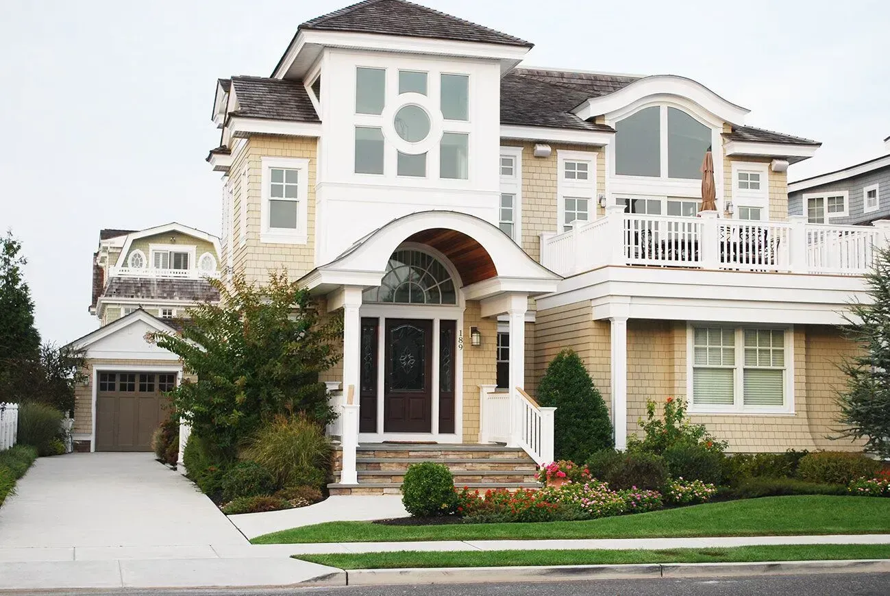 Large cream-colored suburban house with arched entry, white trim, garage, and landscaped front lawn