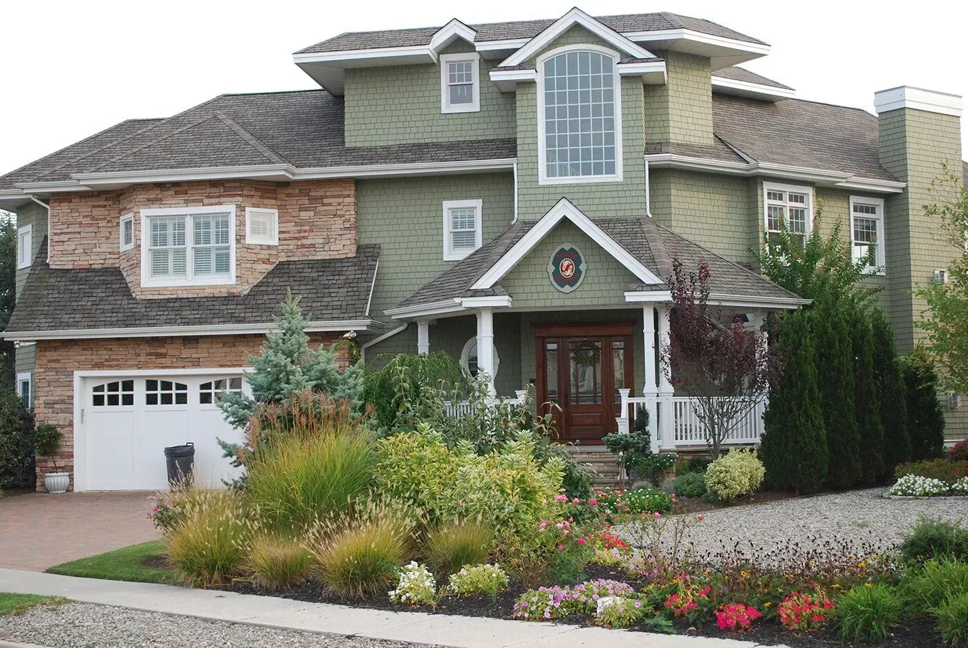 Large suburban house with stone and wood siding, a garage, and landscaped front yard with flowers