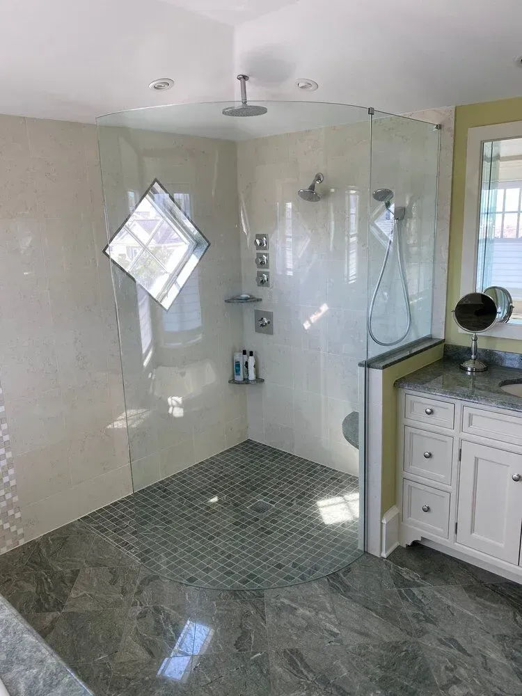 Modern bathroom shower with glass enclosure, gray tile floor, and vanity on the right