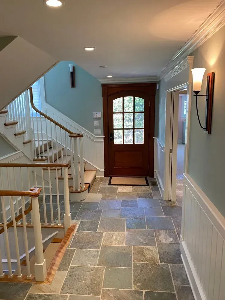 Bright foyer with tiled floor, stairway, white railing, wall sconce, and a wooden front door