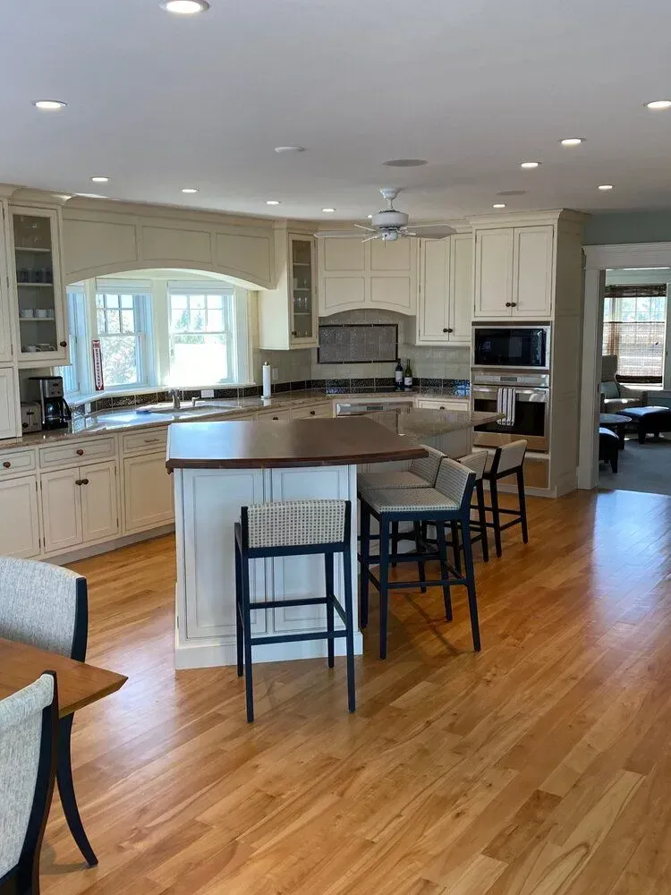 Bright modern kitchen with white cabinets, wood floors, island, stools, and stainless steel appliances
