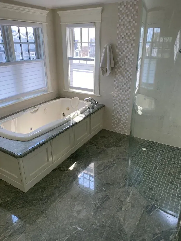 Bright bathroom with a soaking tub, marble floor, tiled walls, and large windows.