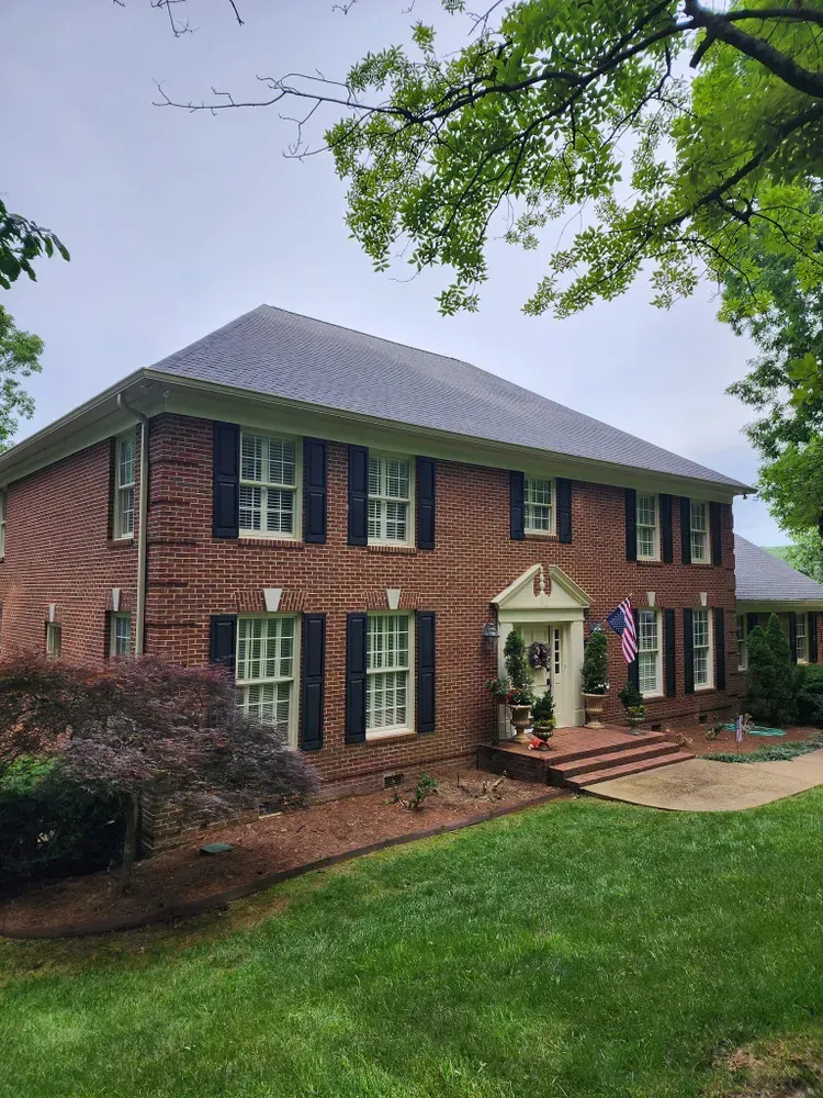 A large brick house with a gray roof and black shutters.