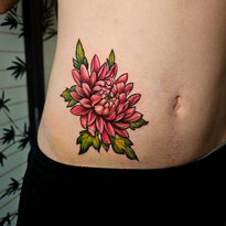 Pink and red chrysanthemum tattoo on a pale abdomen, with green leaves and black clothing.