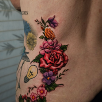 Floral tattoo on torso, red rose with pink, purple, and orange flowers, green leaves.