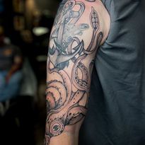 Arm tattoo of an anchor and squid tentacles in black and gray ink.