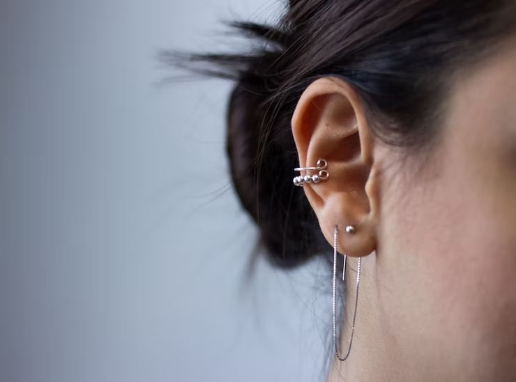 Ear with three piercings: a cuff, a stud, and a long, linear earring.