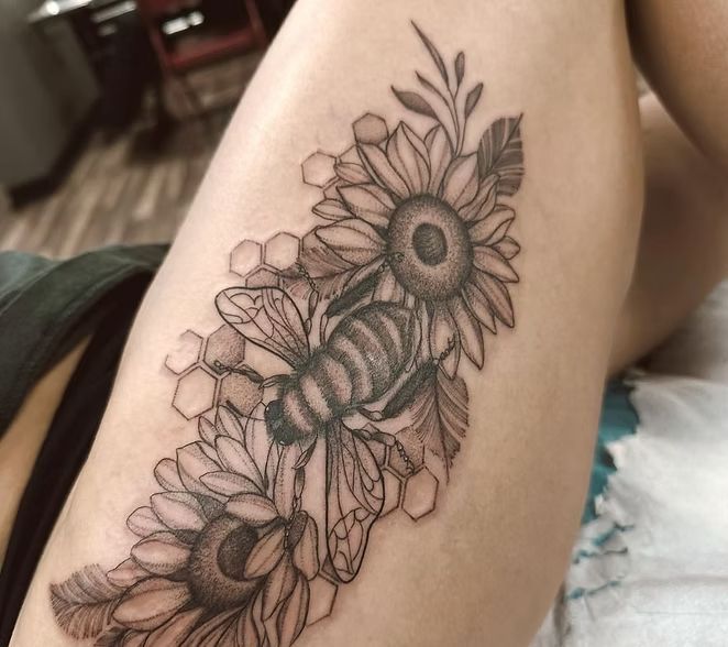 Black and gray bee tattoo with sunflowers and honeycomb on a thigh.