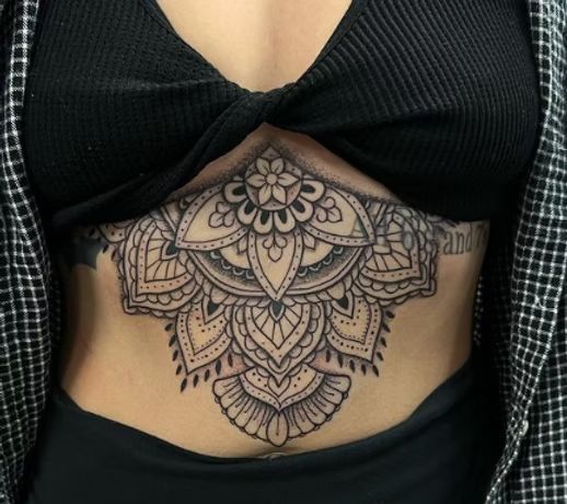 Mandala stomach tattoo on a person wearing a black top and plaid shirt.