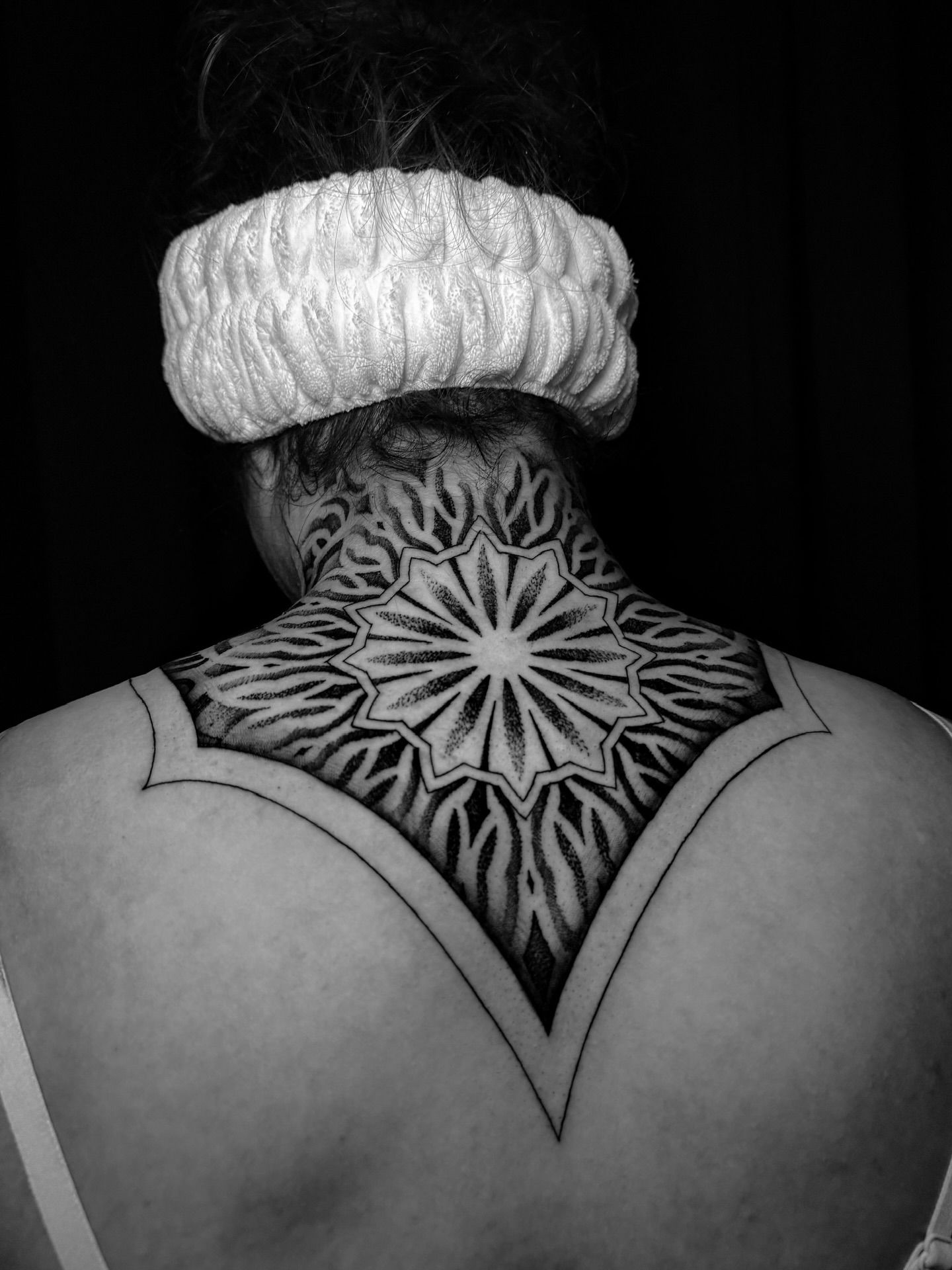 Black and white photo of a person's back. Neck tattoo is a geometric design that extends from the neck to the upper back.
