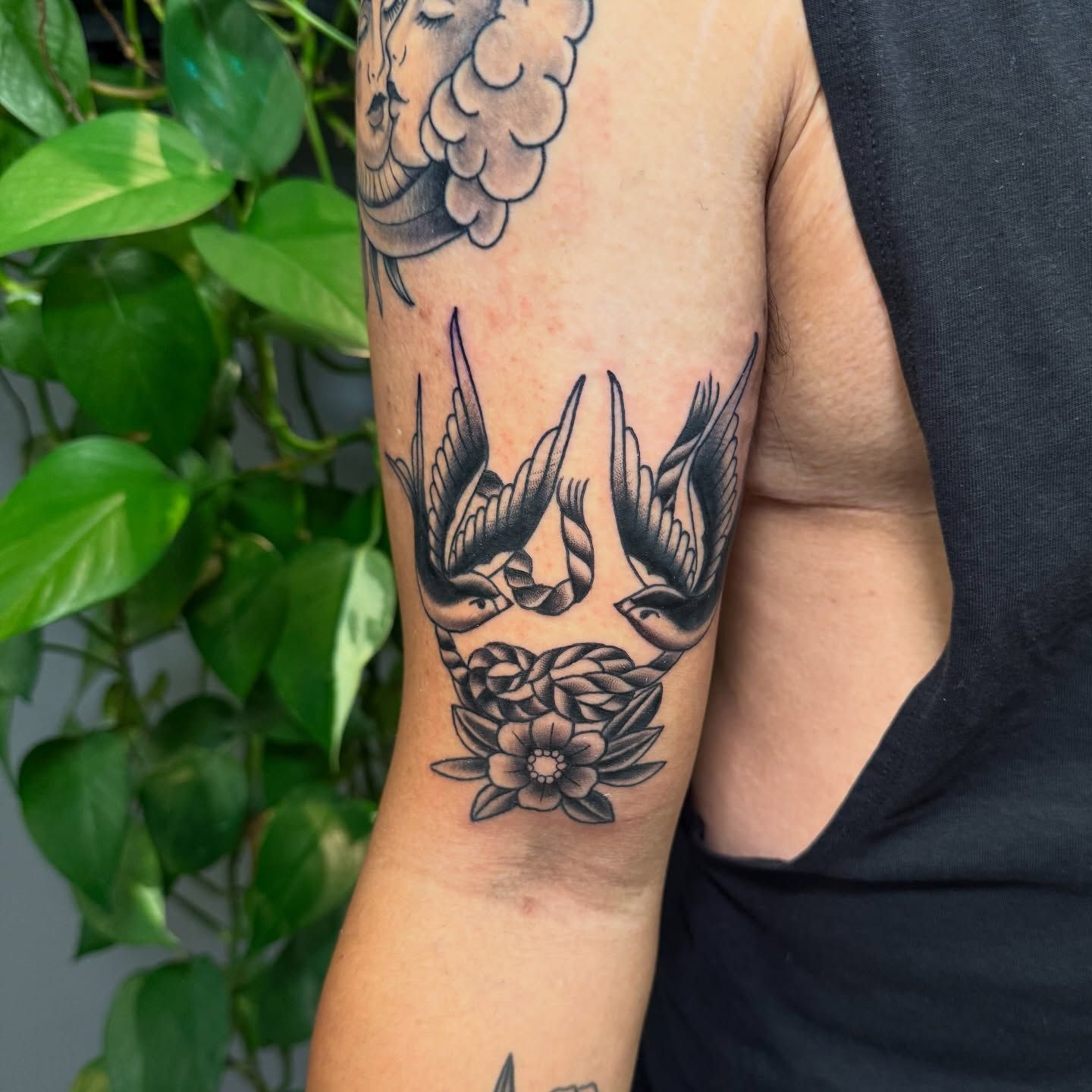 Black and white swallow bird tattoo with ribbon and flower on upper arm.