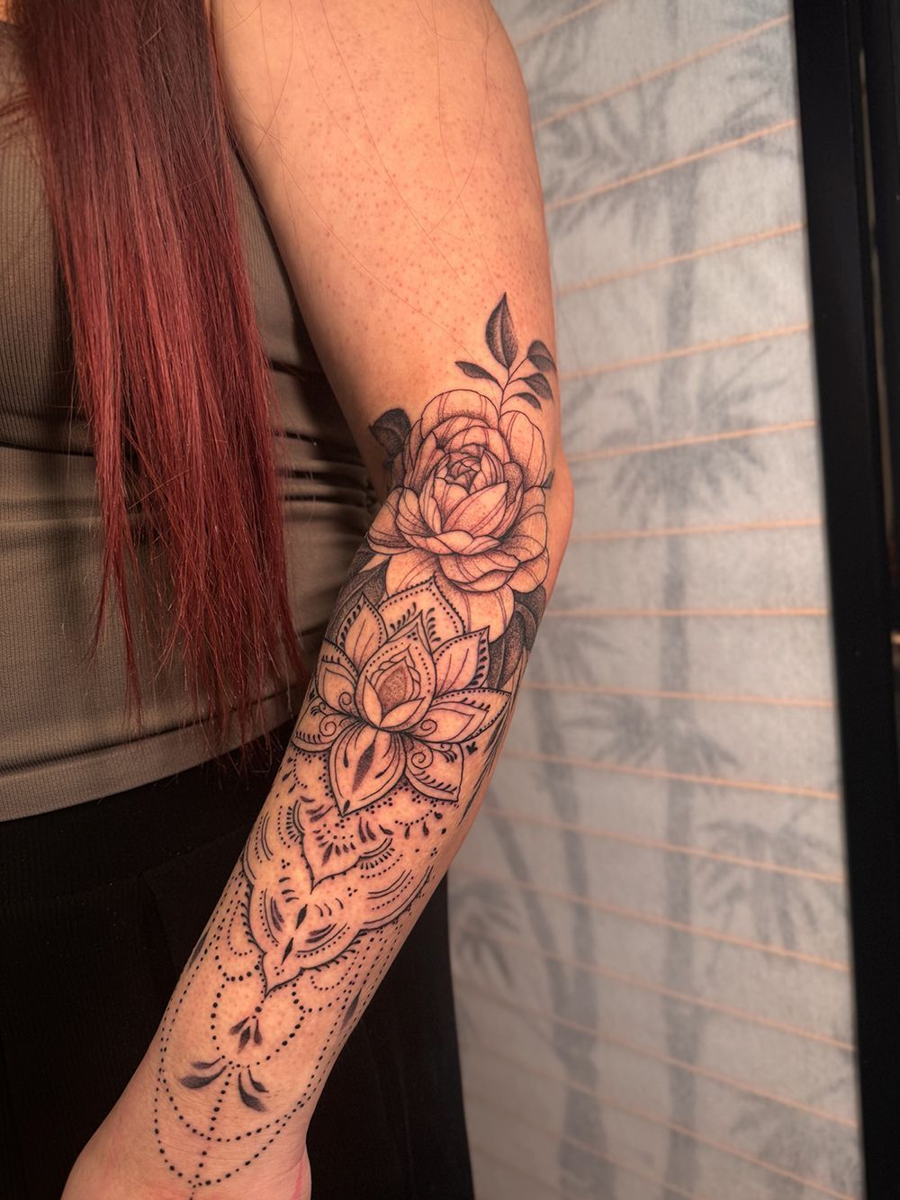 Arm with floral and mandala tattoo in black ink.